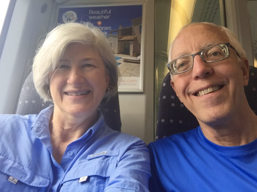 Helen and Wick in hiking clothes sitting on a train to the airport