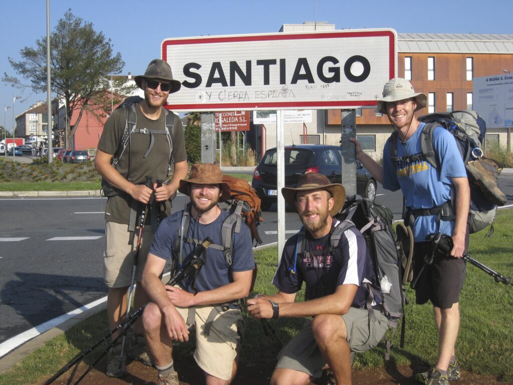 Four Camino pilgrims with Santiago ton sign