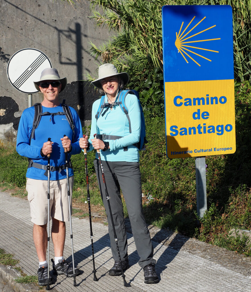 Helen and Wick in hiking clothes standing by a road sign for the Camino de Santiago