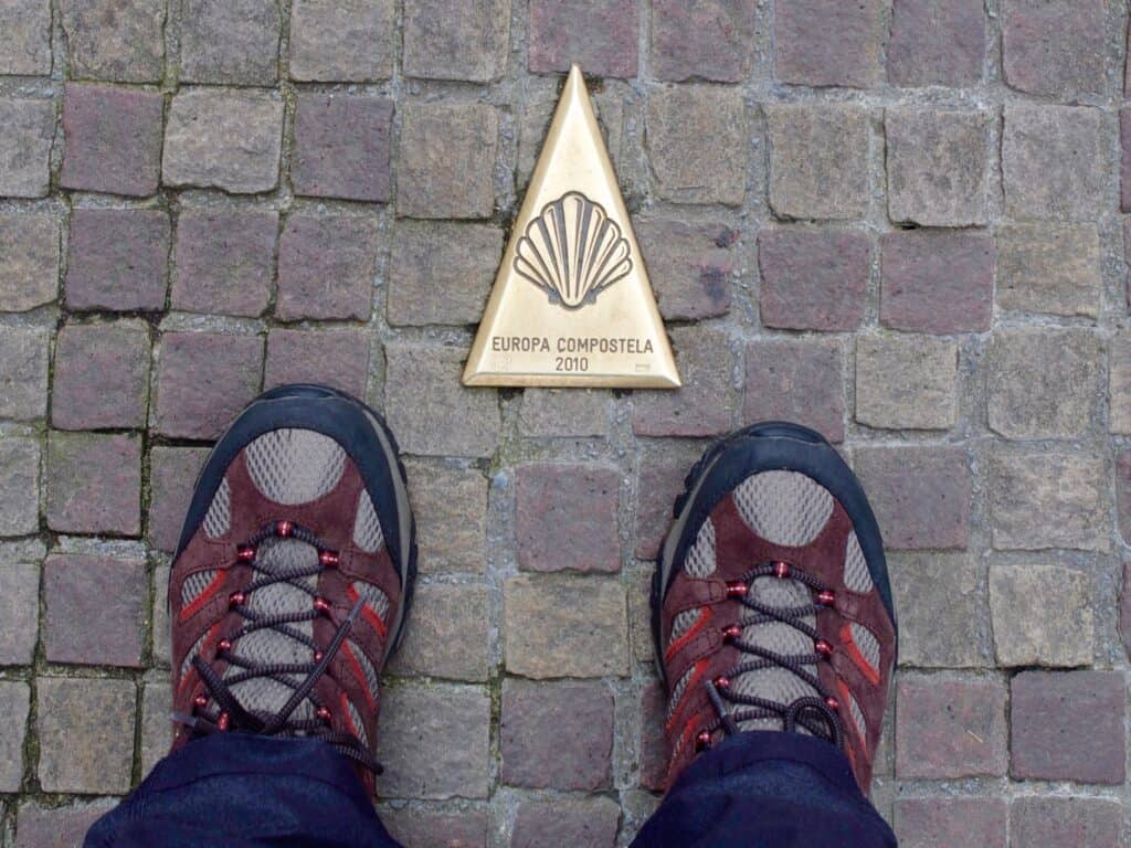 Merrell Moab hiking shoes near a brass Camino waymark on the road in St. Jean Pied-de-Port, France