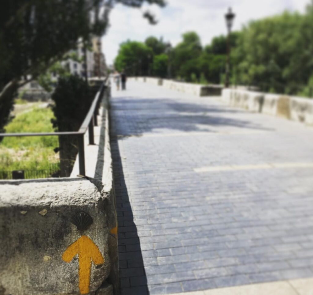 yellow Camino arrow painted on concrete wall in León