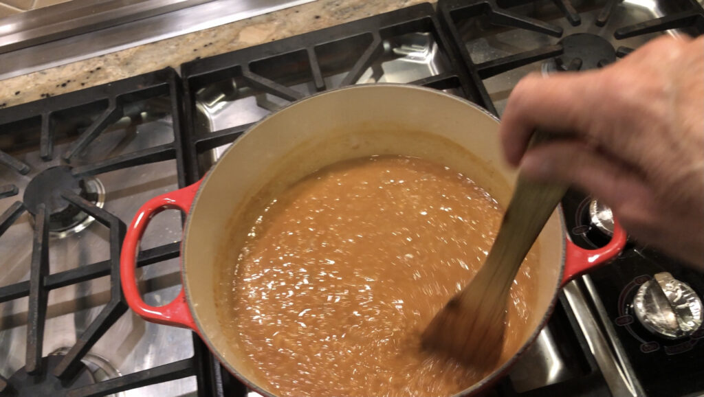 orange soup pot with red lentil soup being stirred with a wooden spoon