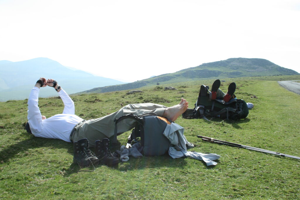 Wick and Hunter lying down in the grass resting with their feet on their packs in the Pyrenees