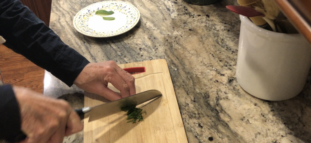 hands holding knife chopping fresh mint on a wooden cutting board