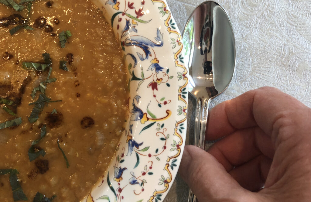 decorative soup bowl with Red Lentil Soup Abastos and a hand gripping a spoon 