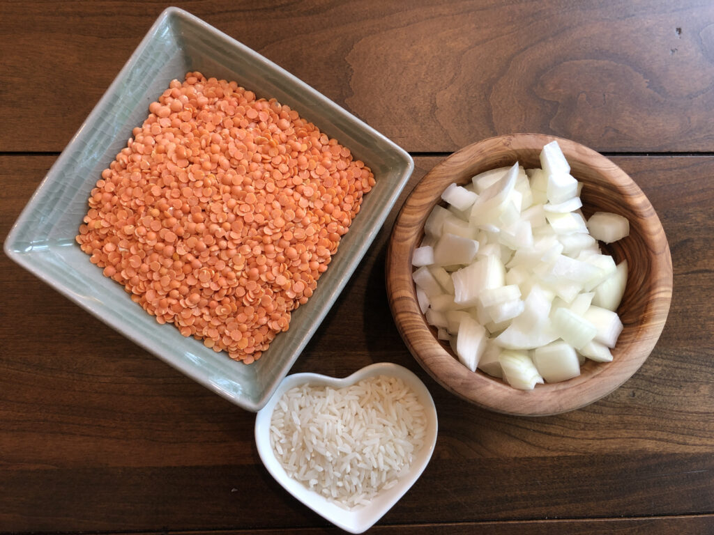 Square bowl of red lentils, wooden bowl with chopped onion and heart shaped bowl with white rice