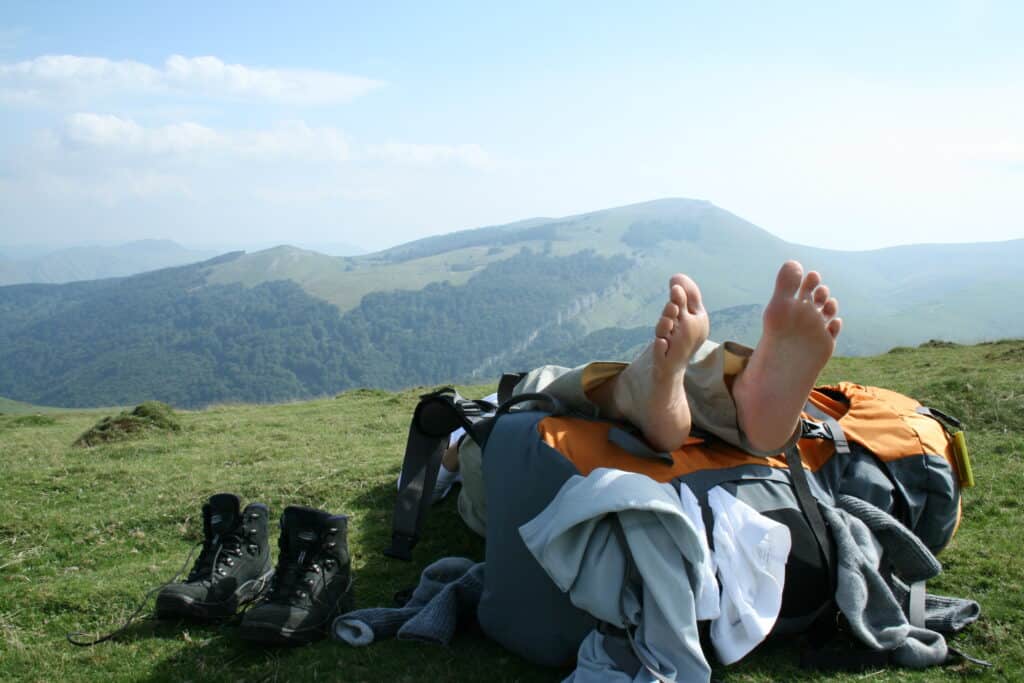 hiker's feet resting on orange backpack with Pyrenees mountains in background Camino de Santiago by Camino Provisions