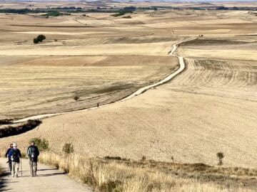 men with backpacks walking on a path through harvested grain fields on the Camino Meseta